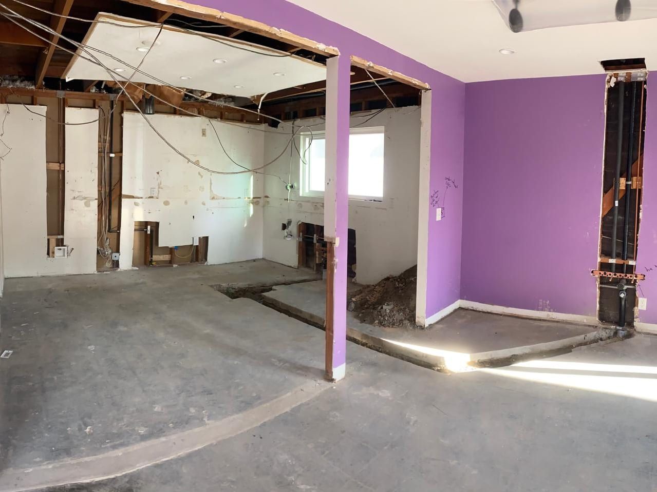 A gutted room with the walls and ceiling opened to the framing and a trench cut across the concrete floor